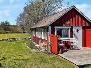 A red wooden cabin with a porch, a small table and chairs, and a view of a field. - 2 Person Holiday Home in Brosarp (Brosarp)