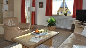 A living room with a sofa, armchair, coffee table, television, and a window with curtains. - Haus Jorg Sosna Modern Retreat (Bad Bayersoien)