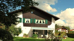 A two-story house with a green awning, a well-maintained lawn, and a garden with flowers and plants. - Haus Jorg Sosna Modern Retreat (Bad Bayersoien)
