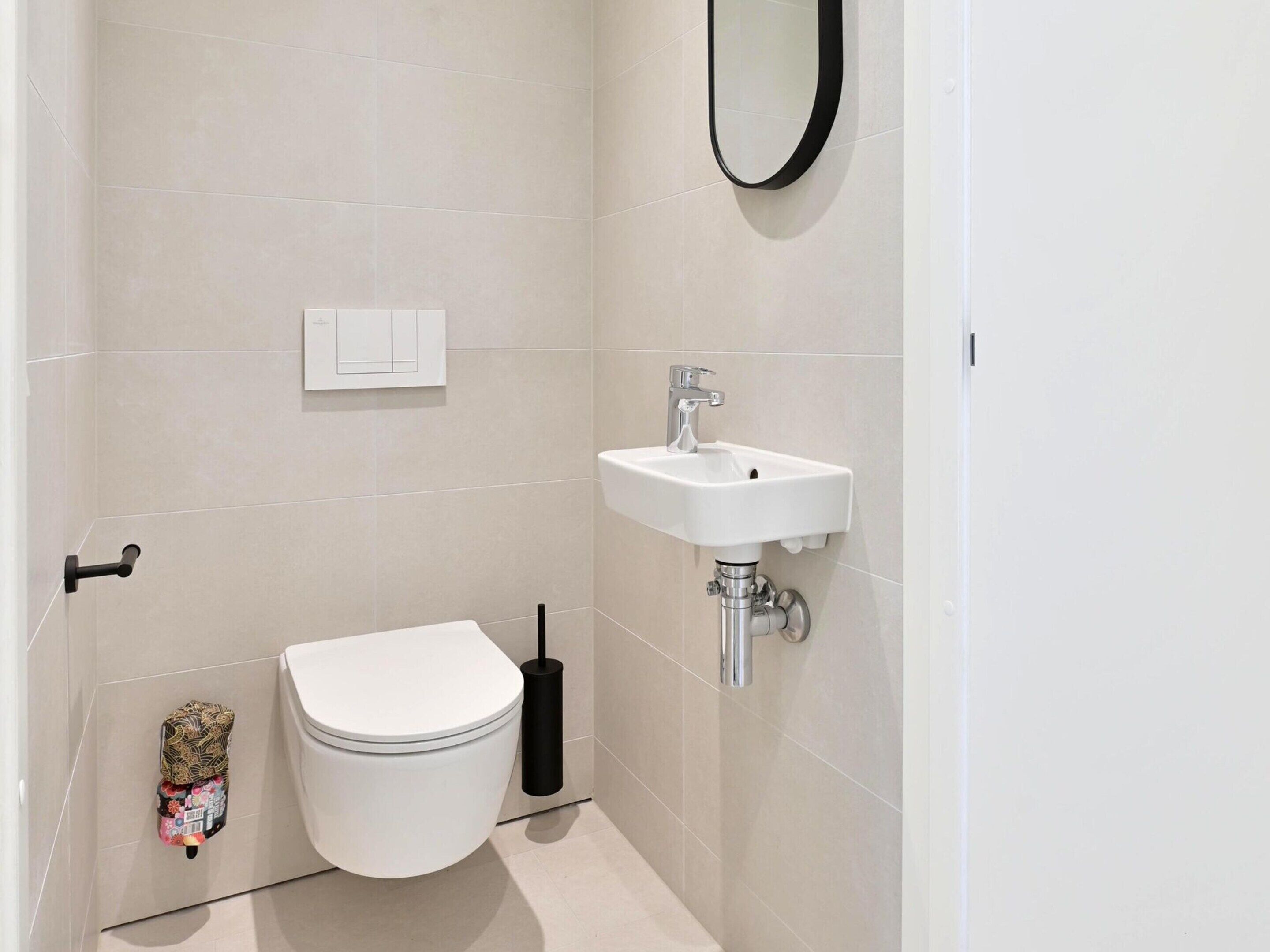 A small, modern bathroom with a toilet, sink, and toilet paper holder.