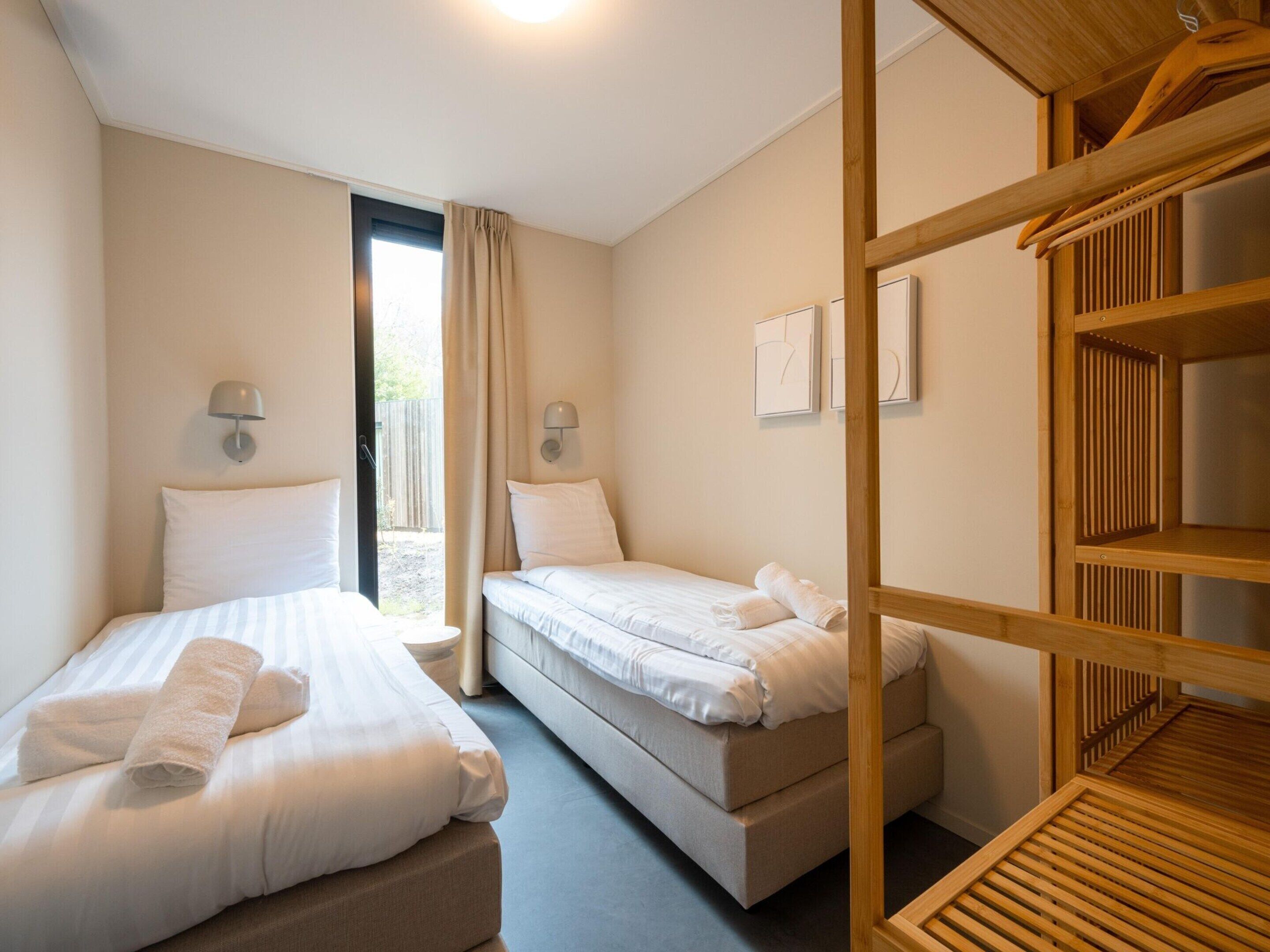 A bedroom with two beds, a wooden bunk bed, a window with curtains, and wall-mounted lamps.