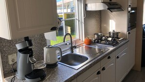 A modern kitchen with a granite countertop, stainless steel appliances, a window with a view of the outside, and a small orange pumpkin on the counter. - Tranquil Chalet Near the Wadden Sea (Tzummarum)