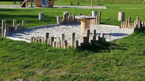 A playground with a wooden play structure, including a slide and swings, surrounded by sand and wooden posts. - Tranquil Chalet Near the Wadden Sea (Tzummarum)