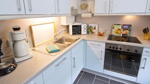 A modern kitchen with white cabinets, a built-in oven, a coffee maker, and a microwave. - Lovely Apartment in Hage (Berumbur)