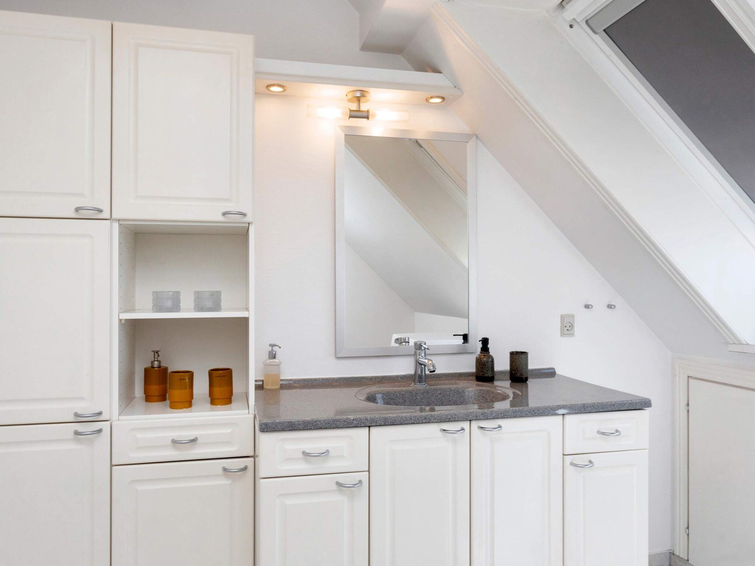 Un baño moderno con muebles blancos, encimera de granito y un espejo grande.