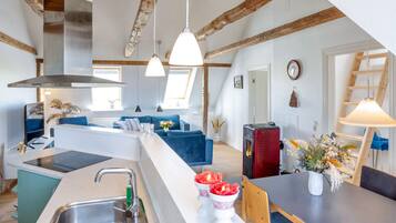 Uma cozinha moderna com ilha central, área de jantar com mesa e cadeiras, e sala de estar com sofá e lareira.