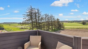 A wooden deck with wicker chairs and a view of a green field and trees. - 4 Star Holiday Home in Thisted (Thisted)