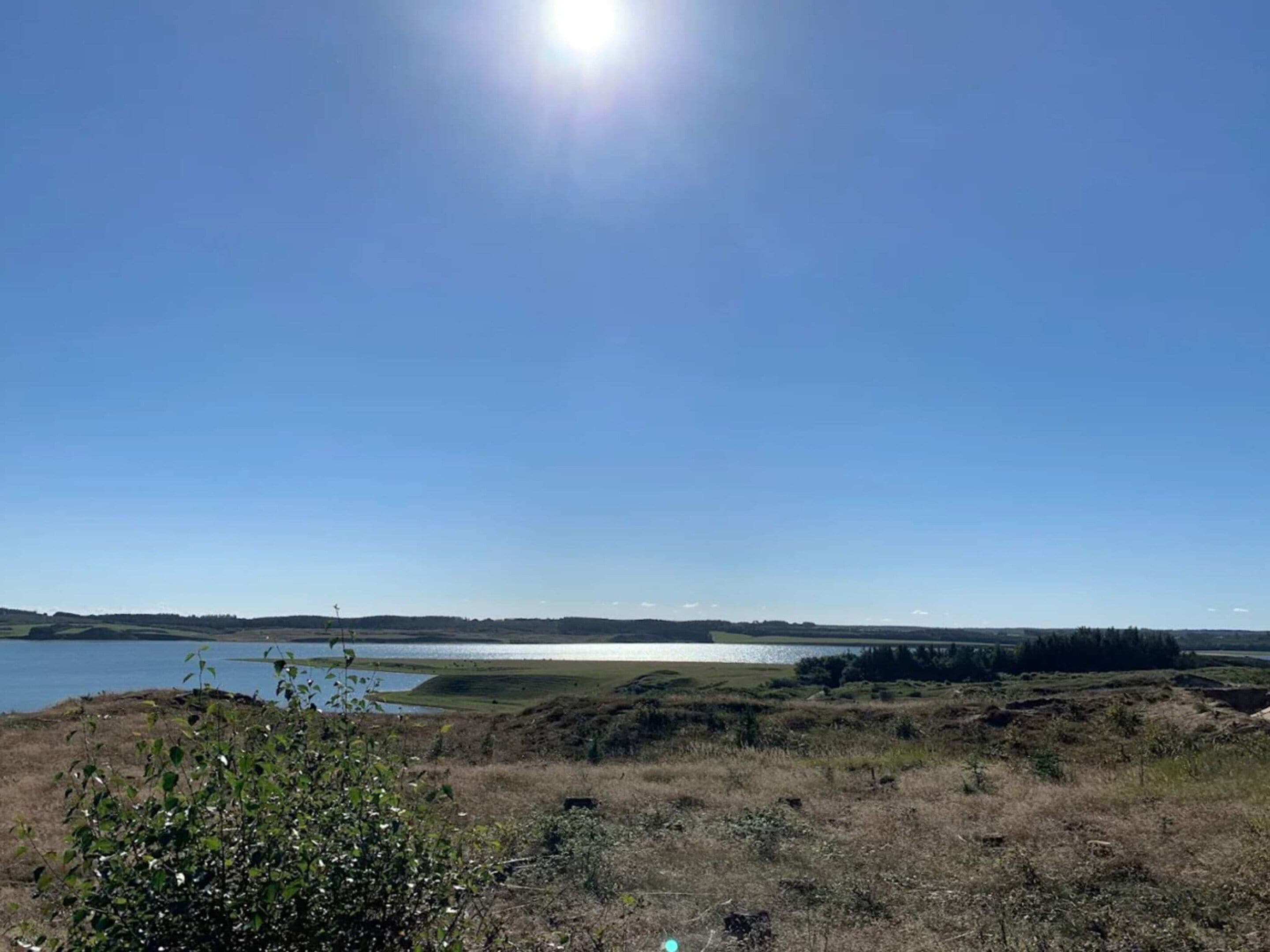 A natural landscape with a body of water, grassy fields, and a clear sky.