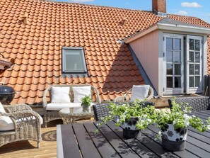 En takterrass med ett tak belagt med tegelpannor, möbler av rotting och krukväxter.