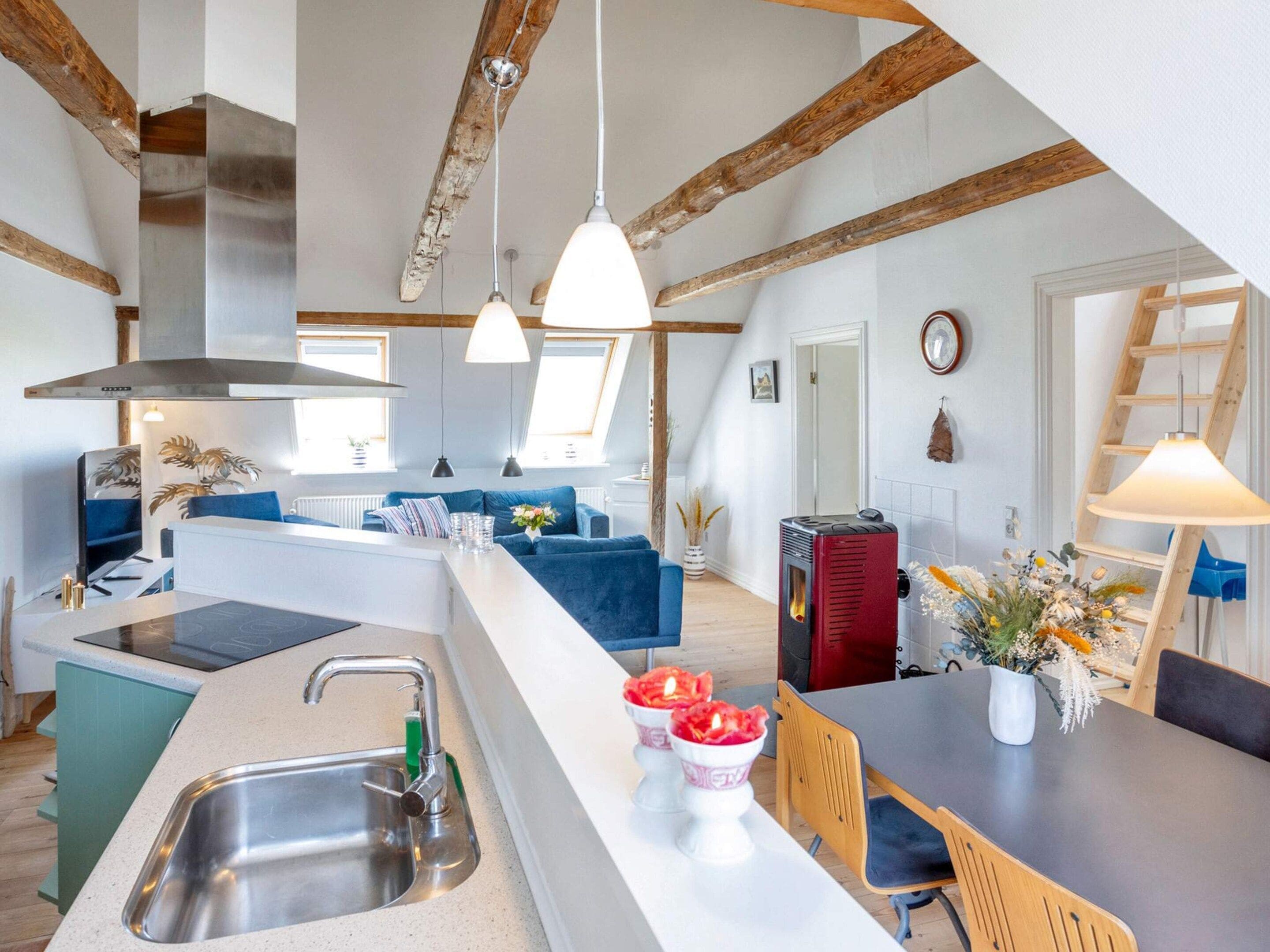 Eine moderne Küche mit einer zentralen Kochinsel, ein Essbereich mit Tisch und Stühlen sowie ein Wohnbereich mit Sofa und Kamin.