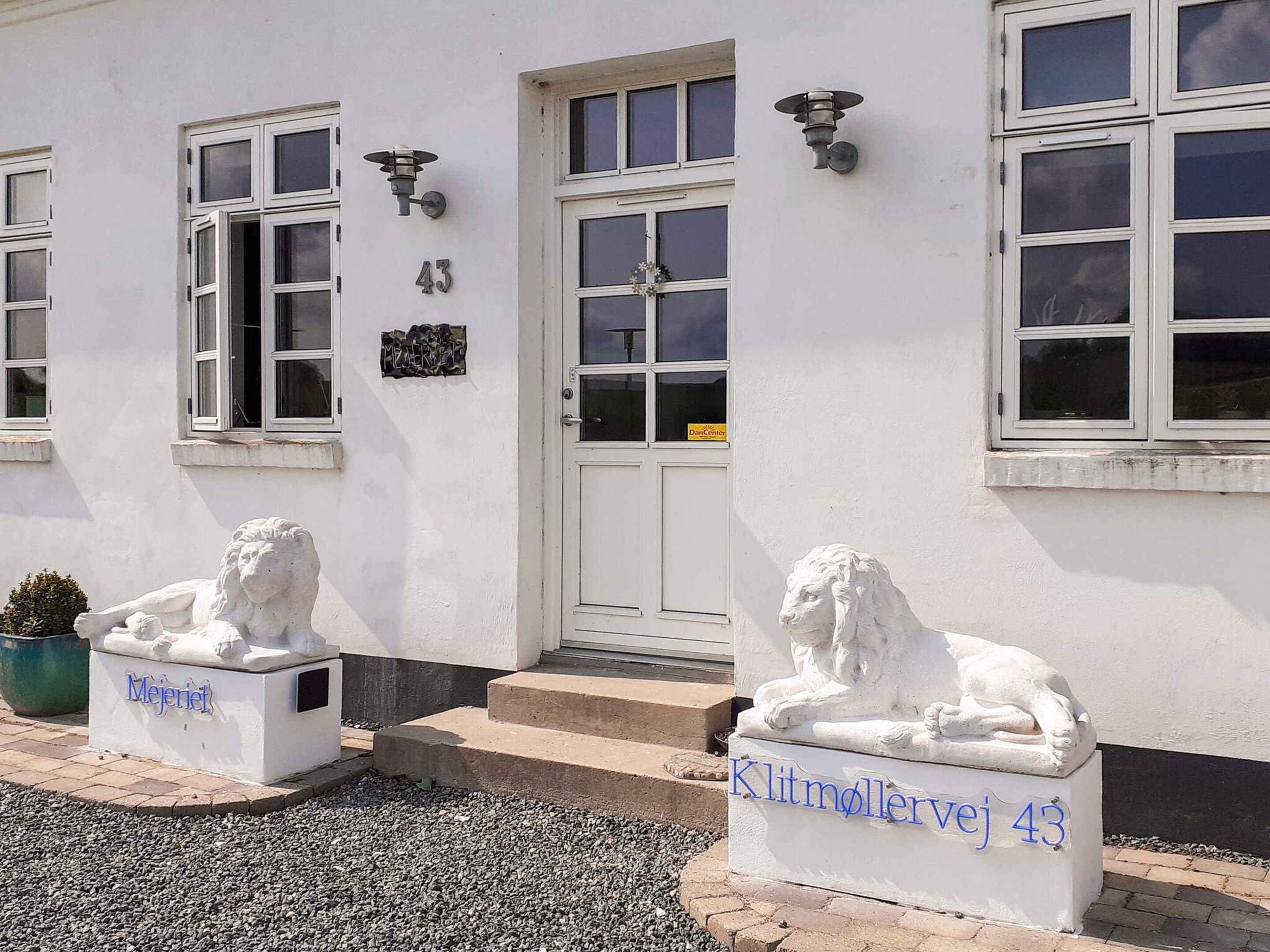 A building with a white facade, numbered 43, featuring two lion statues at the entrance, a door with a glass panel, and a small potted plant.