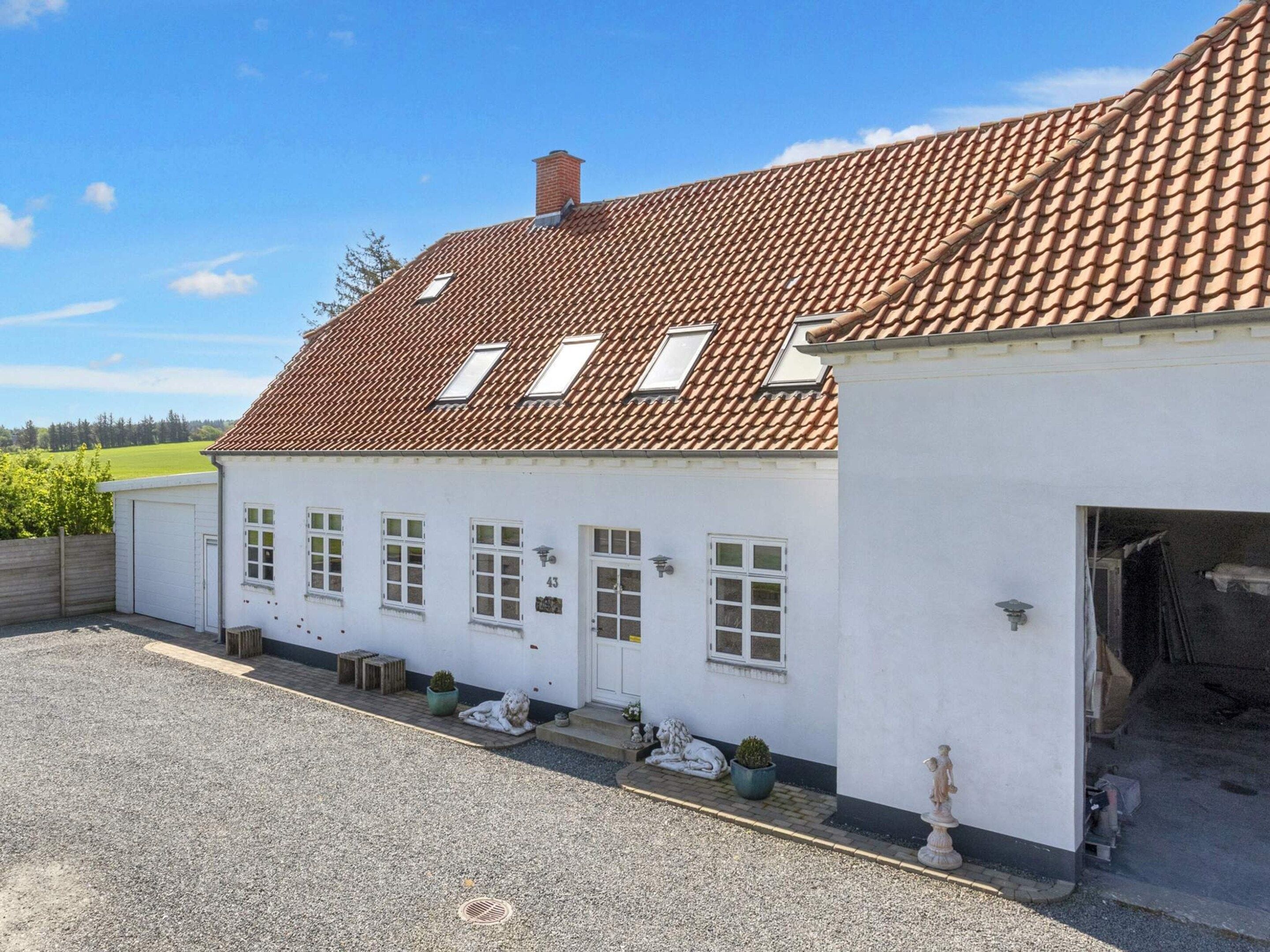 Un bâtiment blanc avec un toit recouvert de tuiles rouges, un garage et une allée gravillonnée.