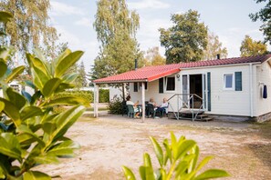 A single-story building with a red-tiled roof, a covered patio area, and a small porch with a few chairs. - Chalet in Leukermeer by the Waterside (Well)