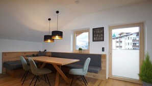 Ein moderner Essbereich mit Holztisch und Stühlen, einer Bank, Pendelleuchten und Blick auf einen Berg durch ein Fenster.