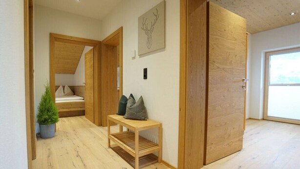 Ein modernes Interieur mit Holzboden, einer Bank mit Kissen, einer kleinen Pflanze und einer Tür zu einem anderen Raum.