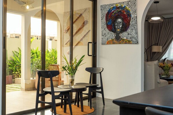 A modern interior with a dining area featuring a glass partition, potted plants, and a large abstract painting. - Château NaNa Willine (Accra)