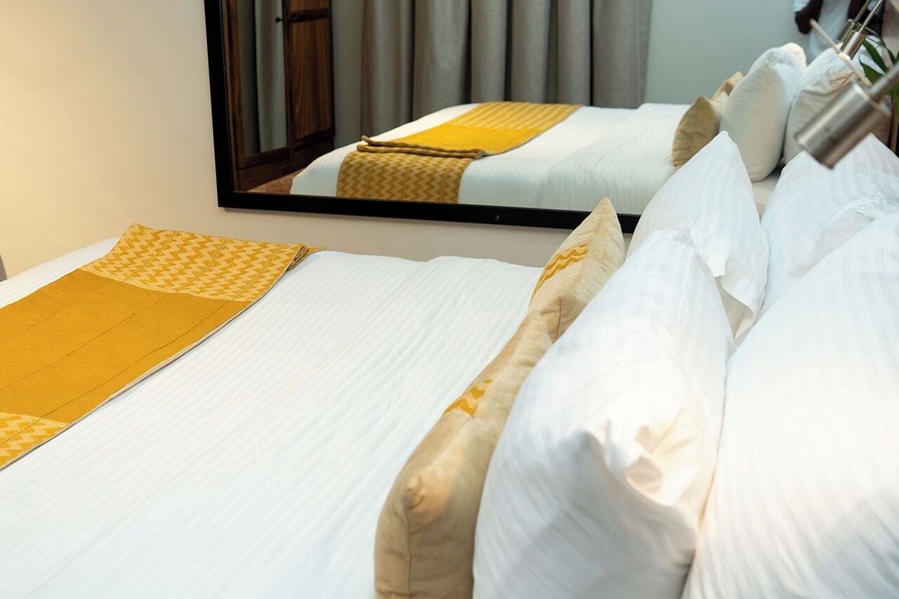 A hotel room with two beds, each with white linens and a yellow patterned bedspread.
