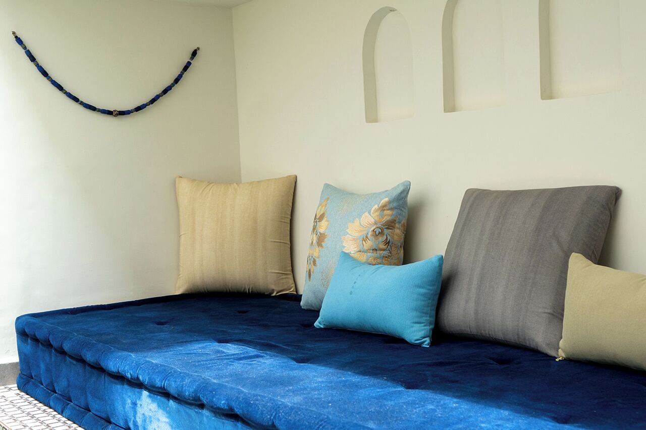 Un lit avec une couverture bleue, des oreillers beige, bleus et gris, et un objet bleu incurvé accroché au mur.