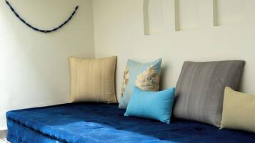 A bed with a blue cover, beige, blue, and gray pillows, and a curved blue object on the wall.