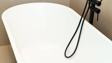 Un bany modern amb una banyera independent, un aixeta negra i un plat de dutxa platejat.
