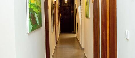 A hallway with wooden doors, framed artwork on the walls, and a light fixture on the ceiling.