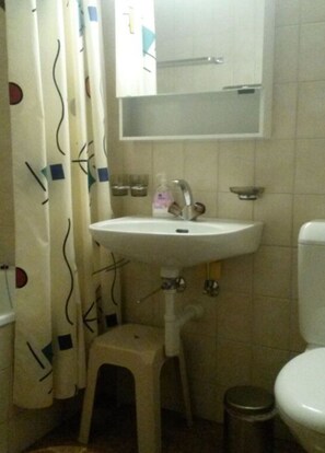 Un baño pequeño con un lavamanos blanco, un espejo encima, un inodoro y una cortina de ducha estampada.