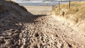 Un sentier de sable qui longe la plage et mène à l’océan, avec des dunes de chaque côté.
