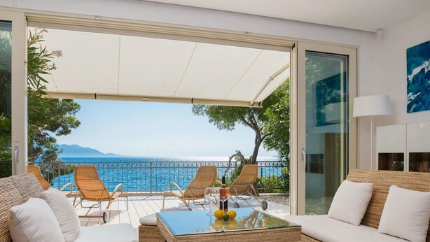 Una sala de estar moderna con una mesa de vidrio, muebles de mimbre y vista al mar.