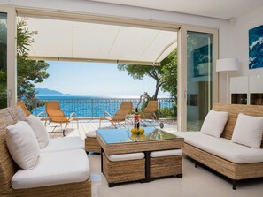 Uma sala de estar moderna com uma mesa de vidro, móveis de vime e vista para o mar.