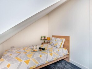 A small, modern bedroom with a sloped ceiling, a wooden bed frame, and a geometric-patterned bedspread. - Bay Retreat Apartment in Skinningrove (Saltburn-by-the-Sea)