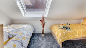 A small, modern bedroom with a skylight, two beds with geometric-patterned bedding, a vase with dried flowers, and a tray with bottles and snacks on one bed. - Bay Retreat Apartment in Skinningrove (Saltburn-by-the-Sea)