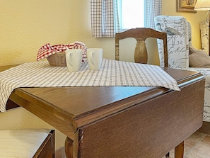 Une table de salle à manger en bois, recouverte d’une nappe à carreaux, avec deux tasses blanches et un panier en osier.