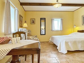 Une pièce confortable avec un lit, une table recouverte d’une nappe à carreaux, une chaise et une lampe.