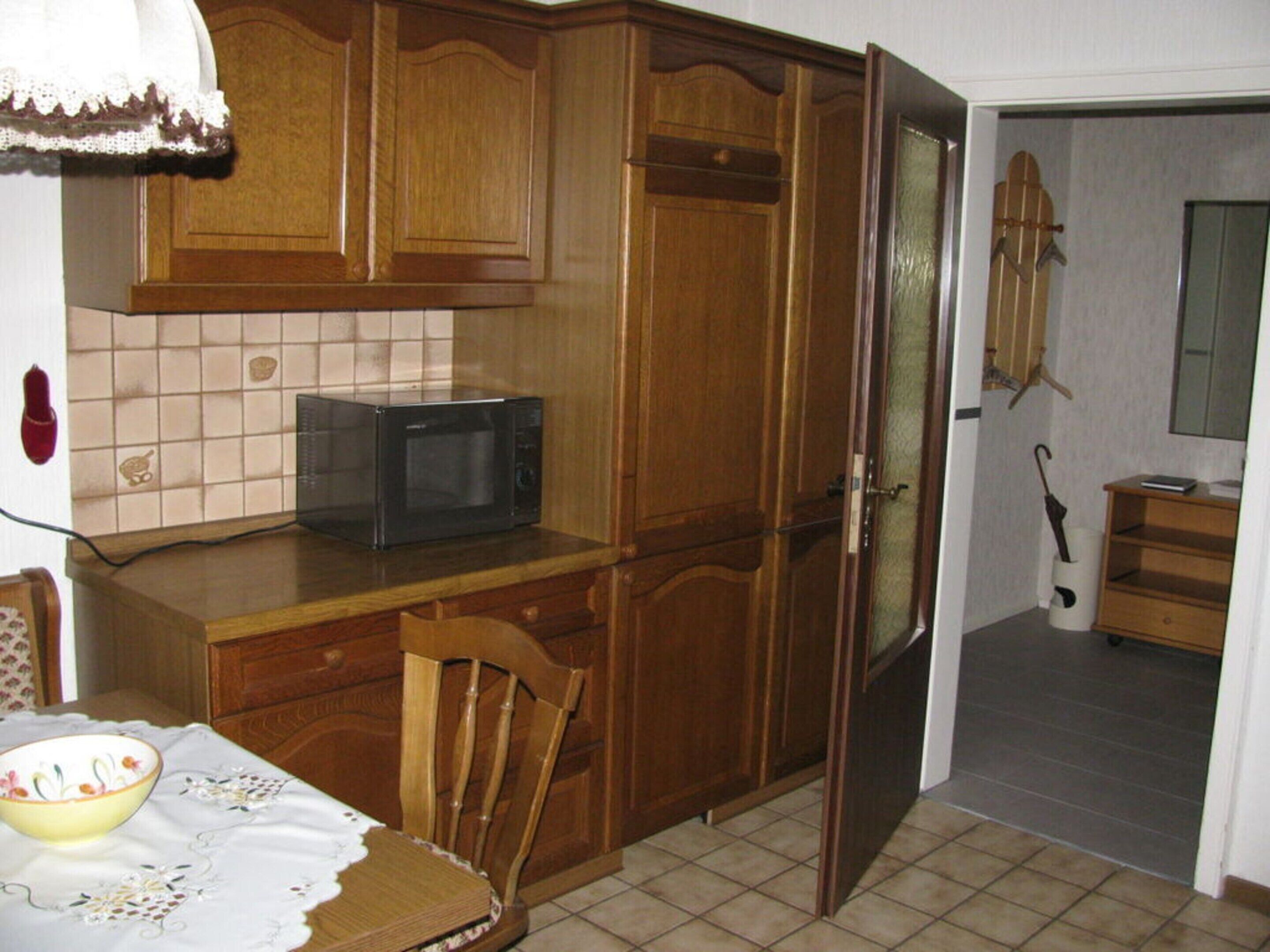 A kitchen with wooden cabinets, a microwave, a chair, and a table with a bowl.