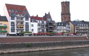 A row of modern and traditional buildings along a riverside, with a prominent tower in the background.