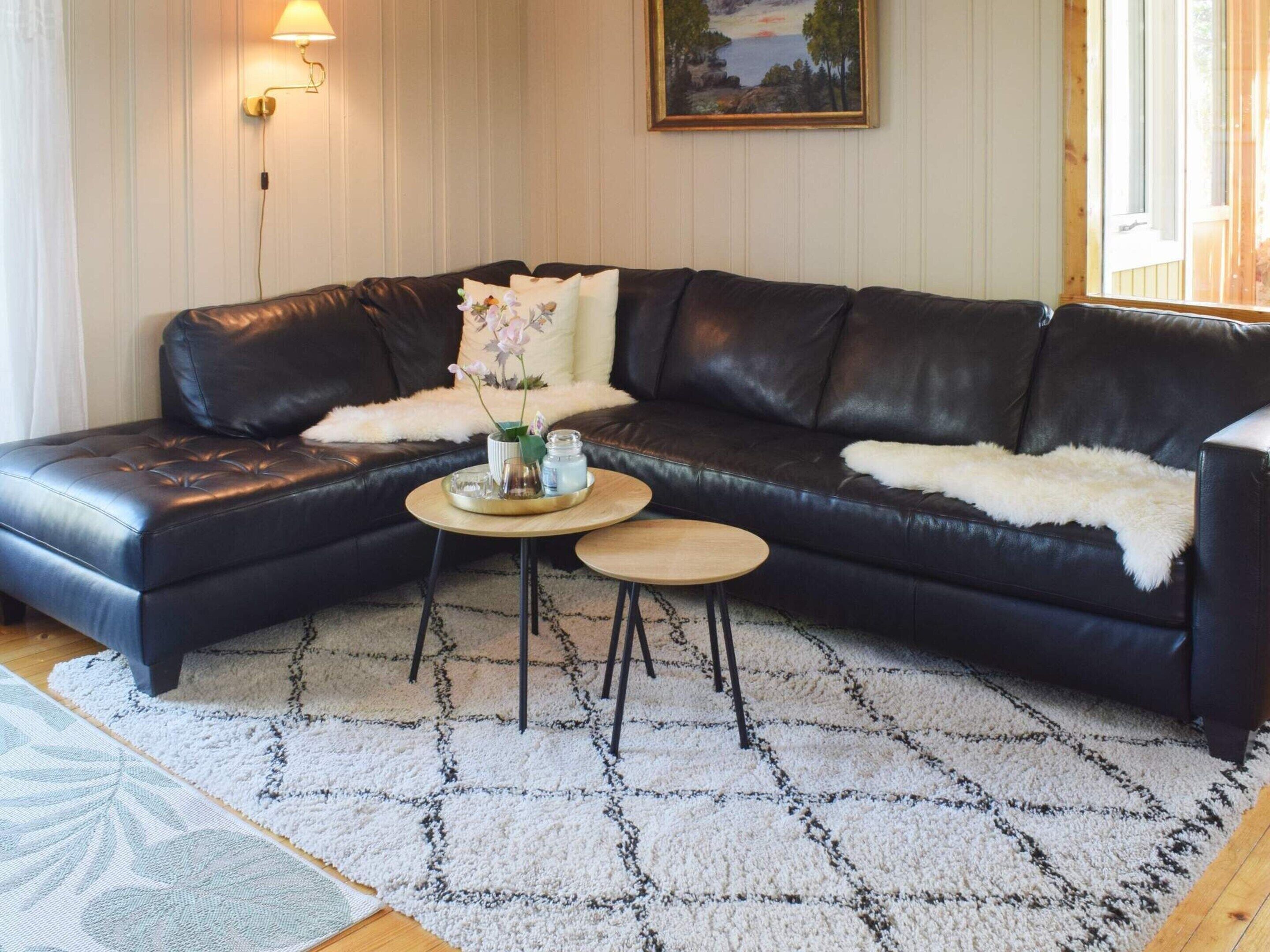 A black leather sectional sofa with a white fur throw, a small round wooden coffee table with a tray, and a white patterned rug.