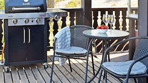 A barbecue grill, two wicker chairs, a small table with a bowl of strawberries and wine glasses, and a wooden deck with a railing. - 4 Star Holiday Home in Halden (Halden)