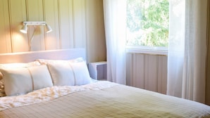A neatly made bed with a quilted cover, a bedside lamp, and a window with sheer curtains. - 4 Star Holiday Home in Halden (Halden)