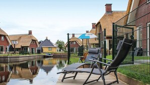 A canal-side deck with two lounge chairs, a wooden walkway, and a row of houses with brick facades and chimneys. - Villa in Friesland With Waterfront Jetty (Idskenhuizen)