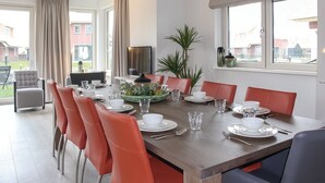 A dining area with a long table set for six, surrounded by red chairs, with a large window providing a view of the outside. - Villa in Friesland With Waterfront Jetty (Idskenhuizen)