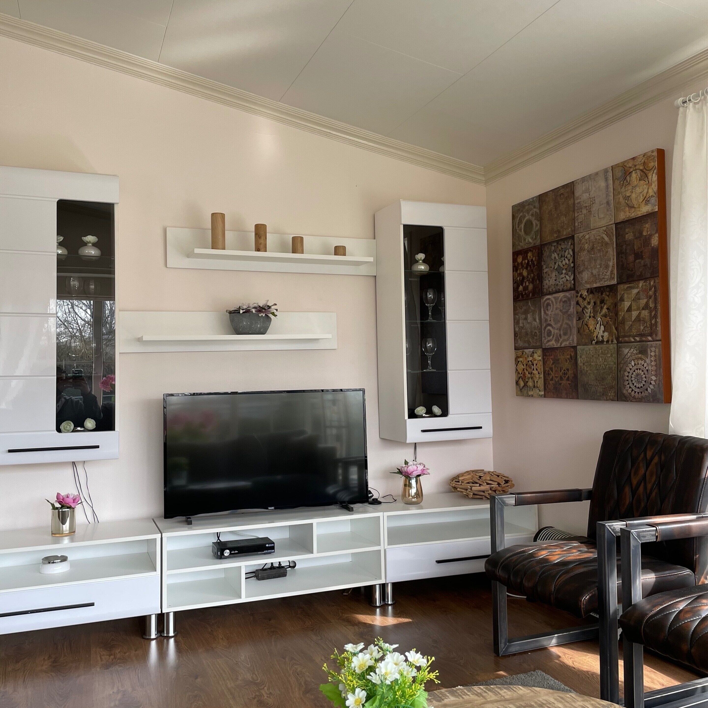 A modern living room with a flat-screen TV, white shelving units, decorative items, and a large abstract art piece on the wall.