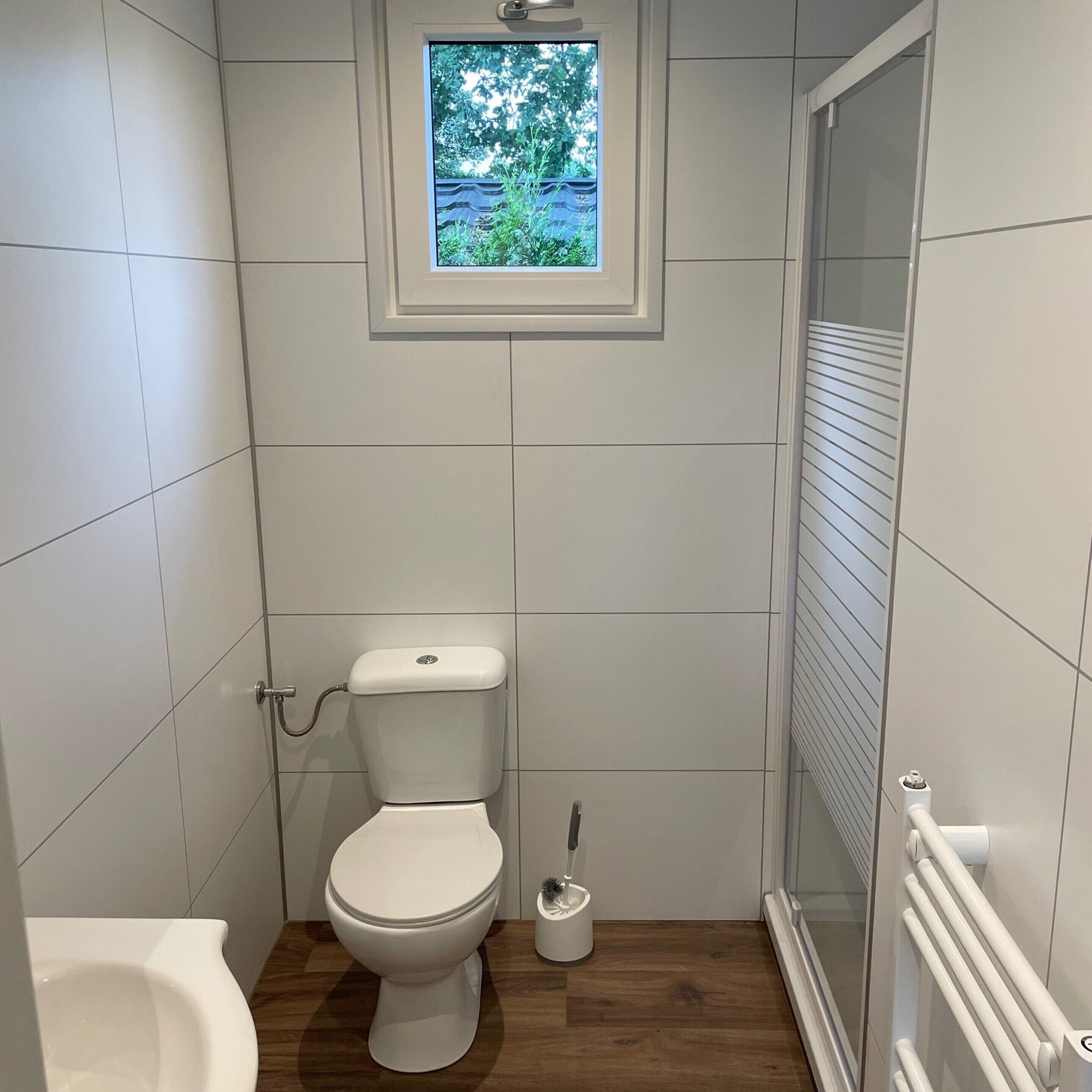 A small, white-tiled bathroom with a toilet, bidet, and a window above the toilet.