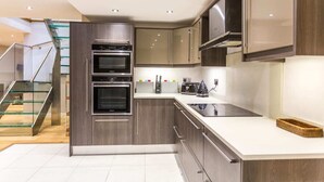 Une cuisine moderne dotée d’appareils électroménagers en acier inoxydable, d’un escalier en verre et d’un plan de travail blanc.