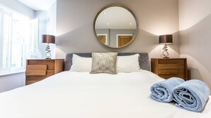 Un lit bien fait, avec du linge de lit blanc, un miroir rond au-dessus et deux lampes de chevet.
