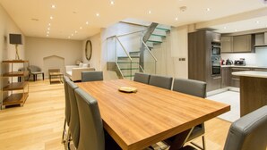 Une cuisine moderne dotée d’appareils électroménagers intégrés, un coin repas avec une table et des chaises en bois, et un escalier avec des rampes en verre.