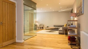Un salon moderne avec un plancher en bois, une cloison en verre, un canapé, une table basse et une bibliothèque.