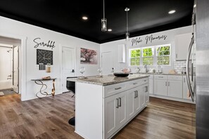 A modern kitchen with white cabinetry, a central island, pendant lighting, and a black ceiling.