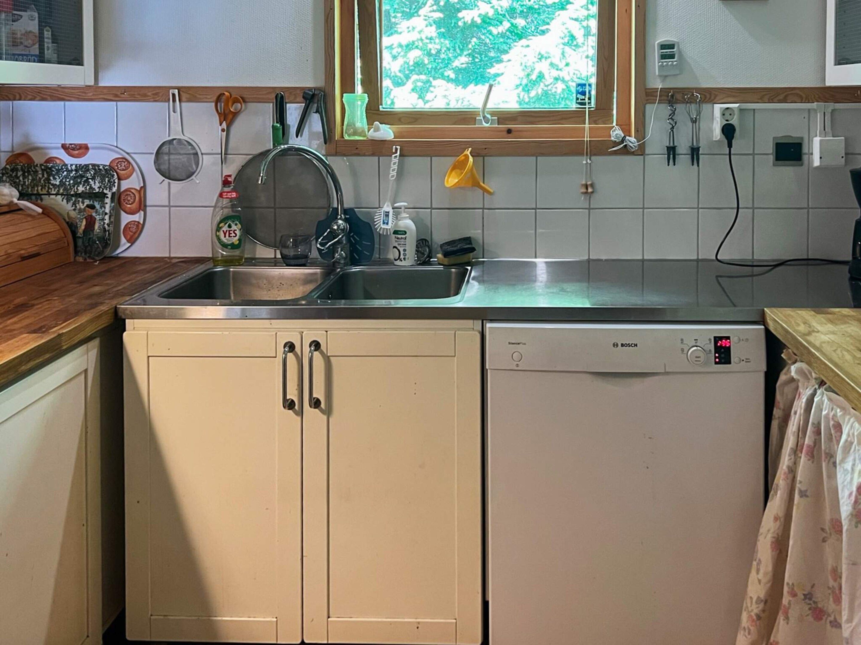 A kitchen with a Bosch dishwasher, a window with a view of greenery, and various kitchen utensils hanging on the wall.
