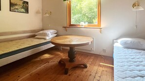A room with a wooden floor, a round table, a window with a polka dot curtain, a bed with a white quilt, and a painting on the wall. - 4 Star Holiday Home in Annerstad (Annerstad)