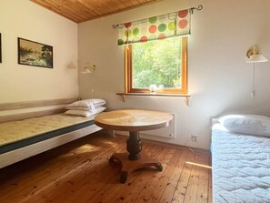 A room with a wooden floor, a round table, a window with a polka dot curtain, a bed with a white quilt, and a painting on the wall. - 4 Star Holiday Home in Annerstad (Annerstad)